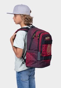 Batoh Harry Potter v tmavě červené barvě s geometrickými vzory, vyšívaným logem, více přihrádkami, černými popruhy a polstrovaným zadním panelem.