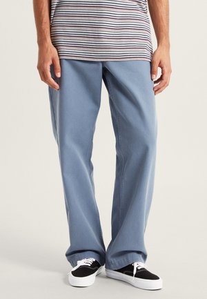 Vaaleansiniset leveälahkeiset farkut, joissa on siisti viimeistely. Yhdistetty mustiin tenniskenkiin ja raidalliseen harmaaseen t-paitaan.