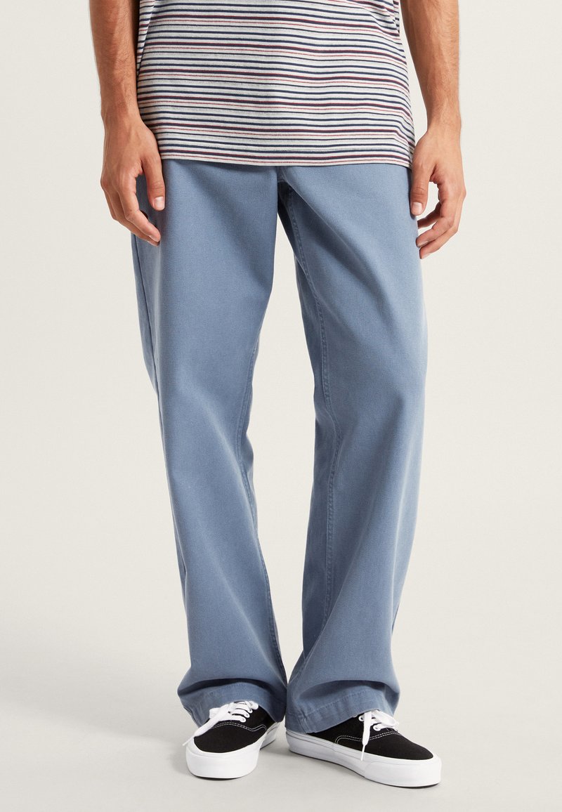 Svetle modré široké džíny vyrobené z denimu, s čistým zpracováním. V kombinaci s černými teniskami a šedým pruhovaným tričkem.