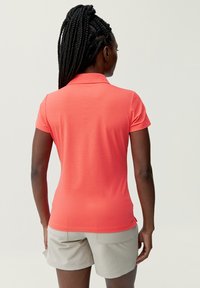 Korala polo z strukturalnym kołnierzykiem, krótkimi rękawami oraz gładką fakturą, w zestawie z jasnoszarymi szortami z widocznymi kieszeniami.