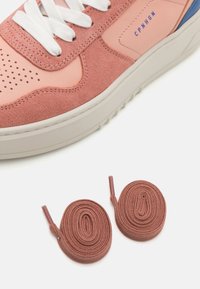 Baskets en daim rose et en cuir avec des détails perforés, lacets blancs, semelle en caoutchouc et deux lacets ronds marron.