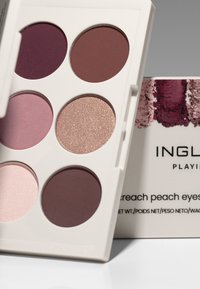 Palette with six eyeshadow shades in varying hues of purple, pink, and glitter, housed in a white case. Includes compact packaging and brand label.