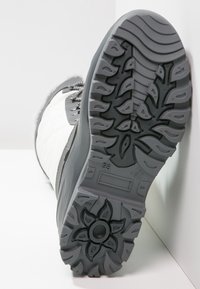 Botín impermeable gris y blanco con suela de goma texturizada que presenta un patrón de flores, cordones y un acabado de pelo sintético en la parte superior.