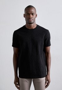 Sort t-shirt med korte ærmer, der har et struktureret mønster, rund hals og en afslappet pasform, der er parret med lyse beige bukser.