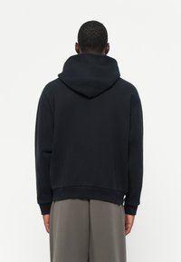 Schwarzer Kapuzenpullover mit gerippten Bündchen und Saum. Weicher Stoff, lockere Passform, sichtbare Nähte und Rückennähte sind vorhanden.