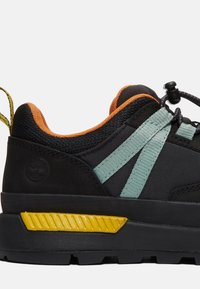 Sneaker nera con accenti verde menta e arancione, tessuto testurizzato, suola in gomma e dettagli gialli distintivi sul tallone.