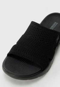 Zwarte instapsandaal met een textuur gebreid bovenwerk en een flexibele rubberen zool, ontworpen voor comfort en ademend vermogen.