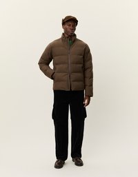 Lett jakke i mørkebrunt med høy krage og glidelås foran. Kombinert med svarte kordfløyels cargo-bukser og mørke sko.