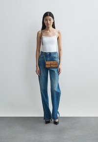 White tank top, high-waisted, light blue denim flared jeans with side slits, tan crossbody bag, and black heels against a neutral background.