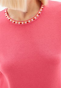 Rosa stickad tröja med en strukturerad yta och rund ringning, utrustad med en dekorativ kant med röda och gula blommönster.