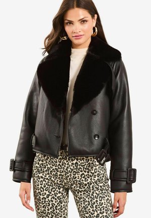 Sort læder cropped jakke med en fluffy krave. Har dobbelt knaplukning og oversized spænder på manchetterne. Bæres over leopardprint bukser.