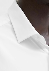 Camicia bianca con colletto classico, tessuto morbido e una sottile lucentezza. Include un dettaglio a bottoni sul colletto e cuciture pulite.