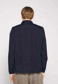 Navy blue, lightweight jacket with a collar, long sleeves, and elastic cuffs. Smooth texture, simple design, no visible hardware or patterns.