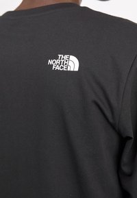Černé bavlněné tričko s krátkým rukávem, s bílým logem "The North Face" na zadní straně nahoře. Hladký povrch, klasický kulatý výstřih.