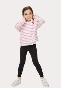 Camisa de manga larga a rayas en blanco y rosa con un detalle de corazón rojo, combinada con leggings negros y zapatillas blancas. Diseño simple y casual.