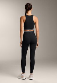 Black athletic crop top and leggings with a fitted design. The top features a contrasting waistband; leggings have a smooth texture and seamless finish.