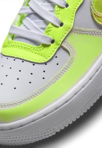 Gros plan d'une basket blanche avec un liseré jaune néon, des lacets blancs, un bout perforé et une semelle blanche texturée.