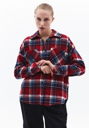 Camicia di flanella a quadri rossa e blu con due tasche sul petto, chiusura con bottoni e maniche lunghe. Tessuto morbido con motivo a scacchi su tutta la superficie.