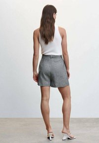Pantaloni corti grigi, sartoriali, con vita alta, cuciture minime e tasche laterali. Indossati con un top bianco e sandali con tacco bianchi.
