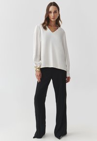 White, V-neck blouse with long, puffed sleeves and a smooth texture, paired with loose-fitting black trousers.