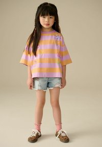 Chemise à manches courtes surdimensionnée rayée lilas et orange avec des motifs brodés ; shorts en denim usés ; chaussettes roses à volants ; chaussures en imprimé léopard brun.