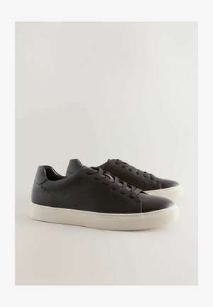 Sneakers in pelle nera con finitura texturizzata, design con lacci, suola in gomma e bordo bianco a contrasto, con discreti dettagli di cucitura.