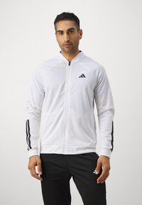 Witte, ritssluiting sportjack met zwarte strepen op de mouwen, gemaakt van glad, lichtgewicht weefsel. Bevat het Adidas-logo op de borst.