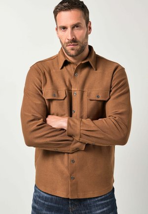 Camisa de franela marrón con cuello abotonado, bolsillos en el pecho y botones a presión. Presenta un acabado texturizado y mangas ajustadas.