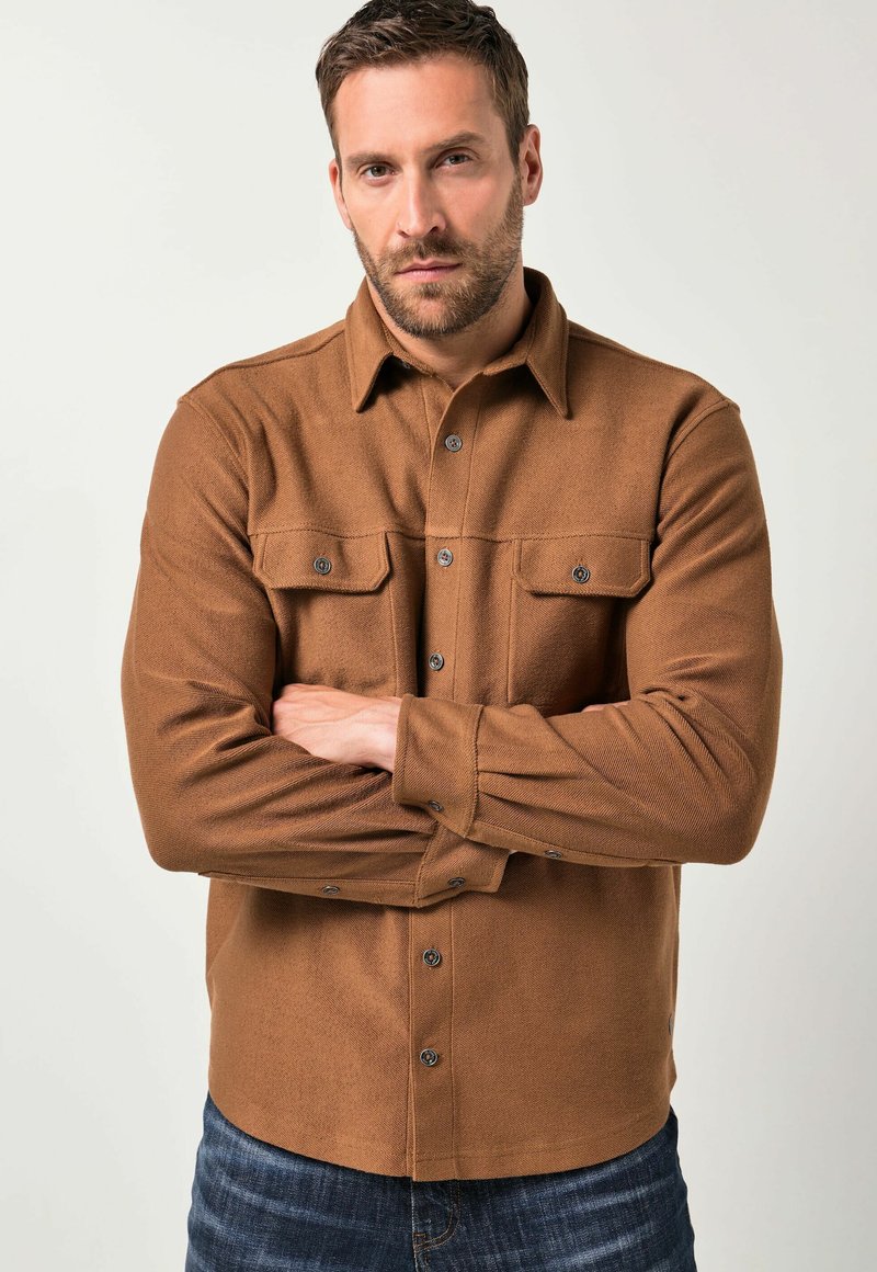 Brun flannel skjorte med knap-ned krave, brystlommer og trykknapper. Har en tekstureret overflade og tætsiddende ærmer.