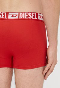Punased puuvillased bokserid valge elastse vöökohaga, millel on "DIESEL" logo. Disainis on ka vormiv lõige ja siledapinnaline materjal.