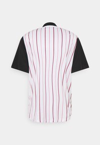 Camicia a maniche corte con un corpo bianco a righe verticali rosse e maniche nere. Il materiale sembra liscio e leggero.