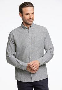 Camicia grigia con bottoni in un tessuto testurizzato, dotata di taschino sul petto, bottoni marroni e maniche lunghe con polsini abbottonati.