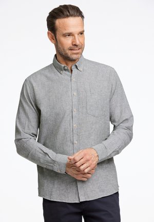 Camisa gris de botonadura en un tejido texturizado, con un bolsillo en el pecho, botones marrones y mangas largas con puños abotonados.
