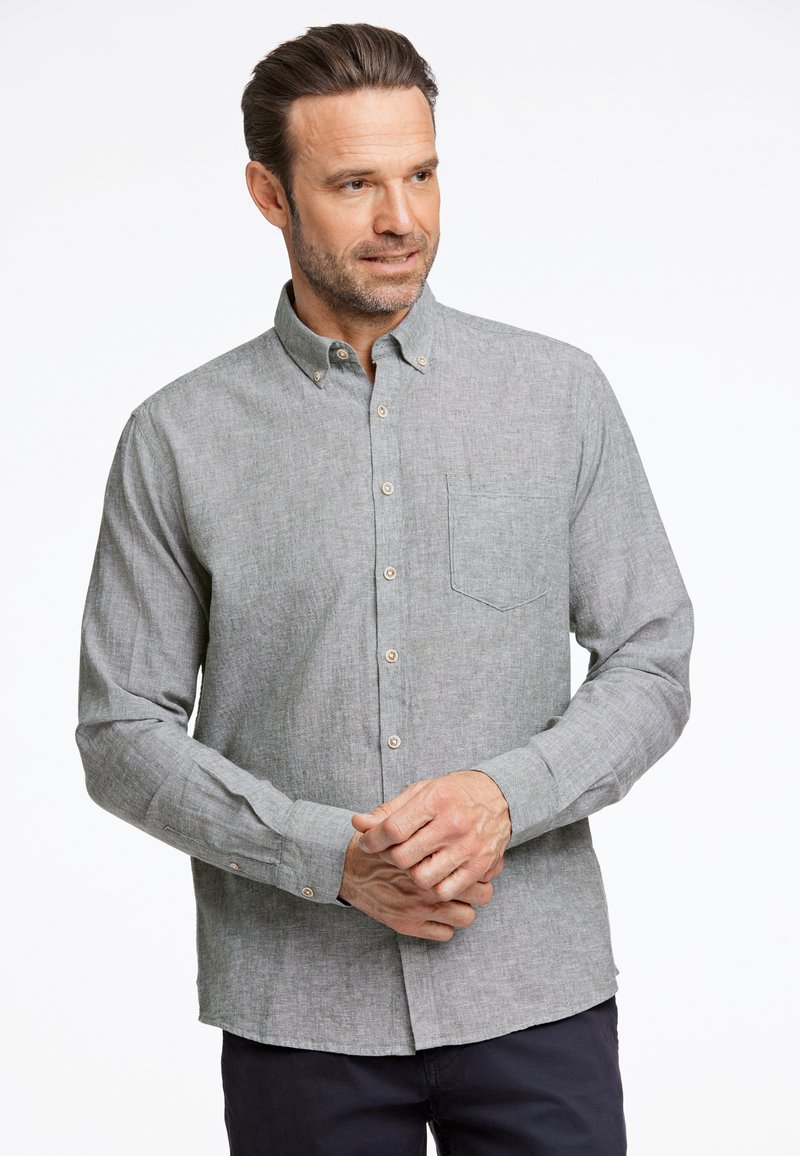 Camicia grigia con bottoni in un tessuto testurizzato, dotata di taschino sul petto, bottoni marroni e maniche lunghe con polsini abbottonati.