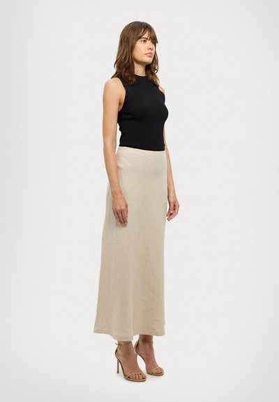 Sort ribbet tanktop uden ærmer, parret med en lys beige lang nederdel, båret med beige højhælede sandaler med stropper, præsenteret mod en neutral baggrund.