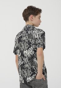 Camicetta a maniche corte, con motivo in bianco e nero e testo in stile graffiti, caratterizzata da una vestibilità ampia e un design con orlo dritto.