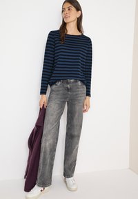 Marineblå og blåstribet langærmet top parret med grå lige ben jeans, hvide sneakers og en lilla sweater draperet over den ene arm.