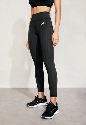 Czarne legginsy z wysokim stanem o teksturowanym wykończeniu, z logo Adidas na lewej udzie oraz płaskimi szwami dla wygody. Czarne buty sportowe.