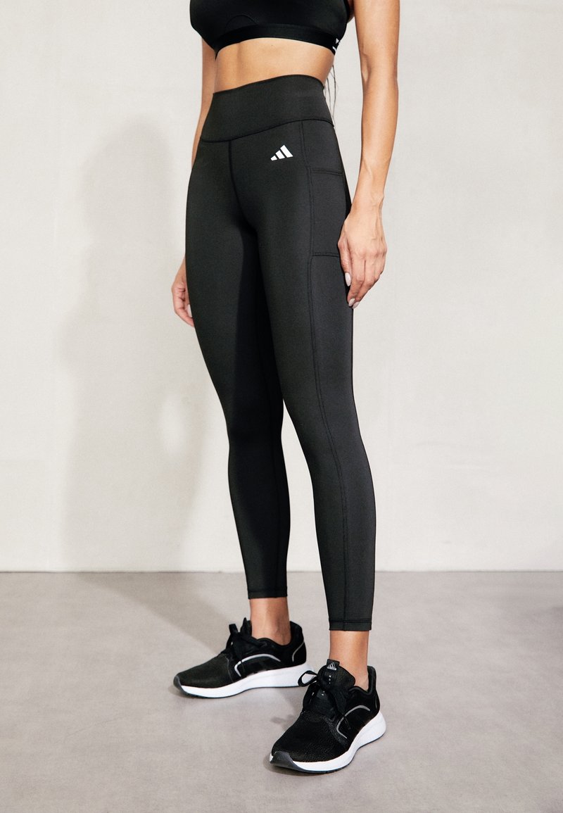 Czarne legginsy z wysokim stanem o teksturowanym wykończeniu, z logo Adidas na lewej udzie oraz płaskimi szwami dla wygody. Czarne buty sportowe.