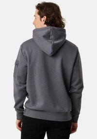 Felpa grigia in cotone con cappuccio regolabile, polsini a costine e tasca laterale con chiusura a scatto. Texture liscia, vestibilità comoda.