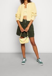 Gul ribbad cardigan, grön kordflorskjol med framknappar, pastellfärgad pärlväska och gröna sneakers med vit detalj.