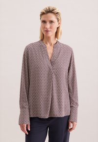 Blusa a maniche lunghe con colletto in un motivo geometrico color bordeaux e crema, realizzata in un tessuto leggero con una vestibilità morbida.