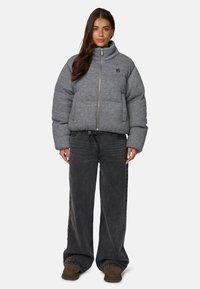 Szara puchowa kurtka z wysokim kołnierzem, zamek błyskawiczny i kieszenie z przodu. Połączona z czarnymi spodniami o szerokich nogawkach i brązowym obuwiem.