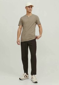 Camisa bege de manga curta com decote em V, calças slim-fit pretas e ténis brancos com riscas castanhas. Design simples, textura suave.