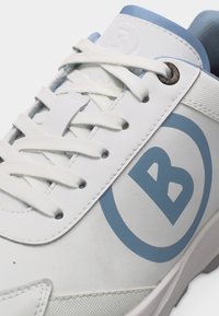 Baskets blanches avec logo "B" bleu, lacets blancs et œillet métallique sur une semelle de couleur claire.