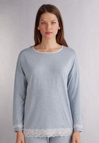 Jasnoniebieski longsleeve wykonany z miękkiego materiału, z białym koronkowym wykończeniem na dole i przy mankietach. Okrągły dekolt z białym akcentem.