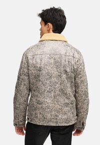 Brun faux læderjakke med en beige faux shearling krave, tekstureret finish og knapdetaljer. Bagfra ses detaljeret syning.