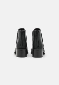 Botas de cuero negras hasta el tobillo con una textura suave, cierre de cremallera en la parte trasera y un tacón en bloque apilado.