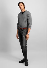 Grå v-hals genser, mørke jeans, brun lærbelte og svarte ankelstøvler. Modellen står med avslappede armer, teksturen på stoffet synlig.