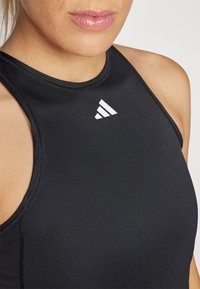 Crna atletska majica bez rukava s visokim izrezom i glatkom teksturom; sadrži bijeli adidas logo na prednjem dijelu.